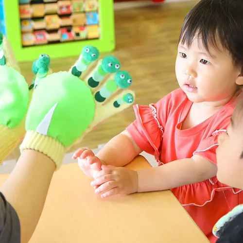 先生の話を聞く園児たち。人形をつけた手袋を用いて、お話をしている。